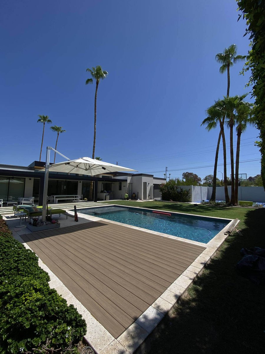 A sleek poolside deck surrounded by lush greenery and palm trees, built by Crosby Home Services in Prescott, AZ